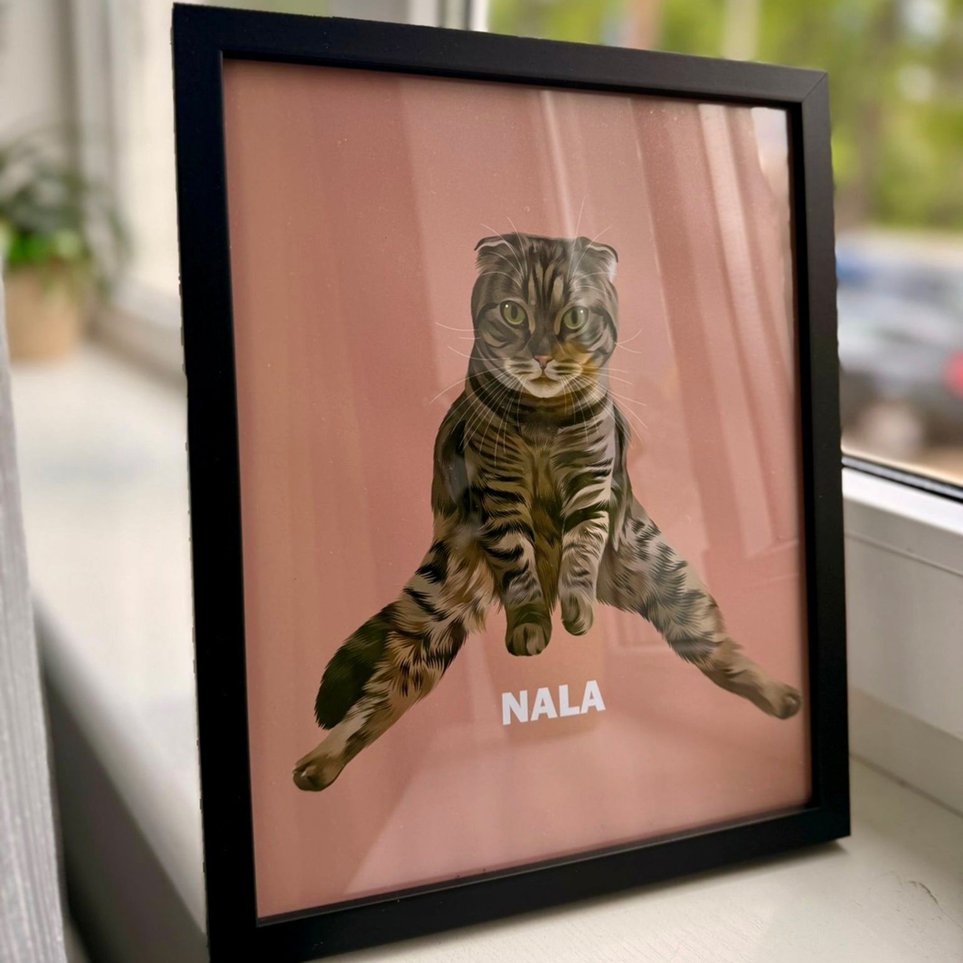 Close up photo of dusty pink custom pet portrait framed poster with black frame featuring artwork of a brownish cat called Nala