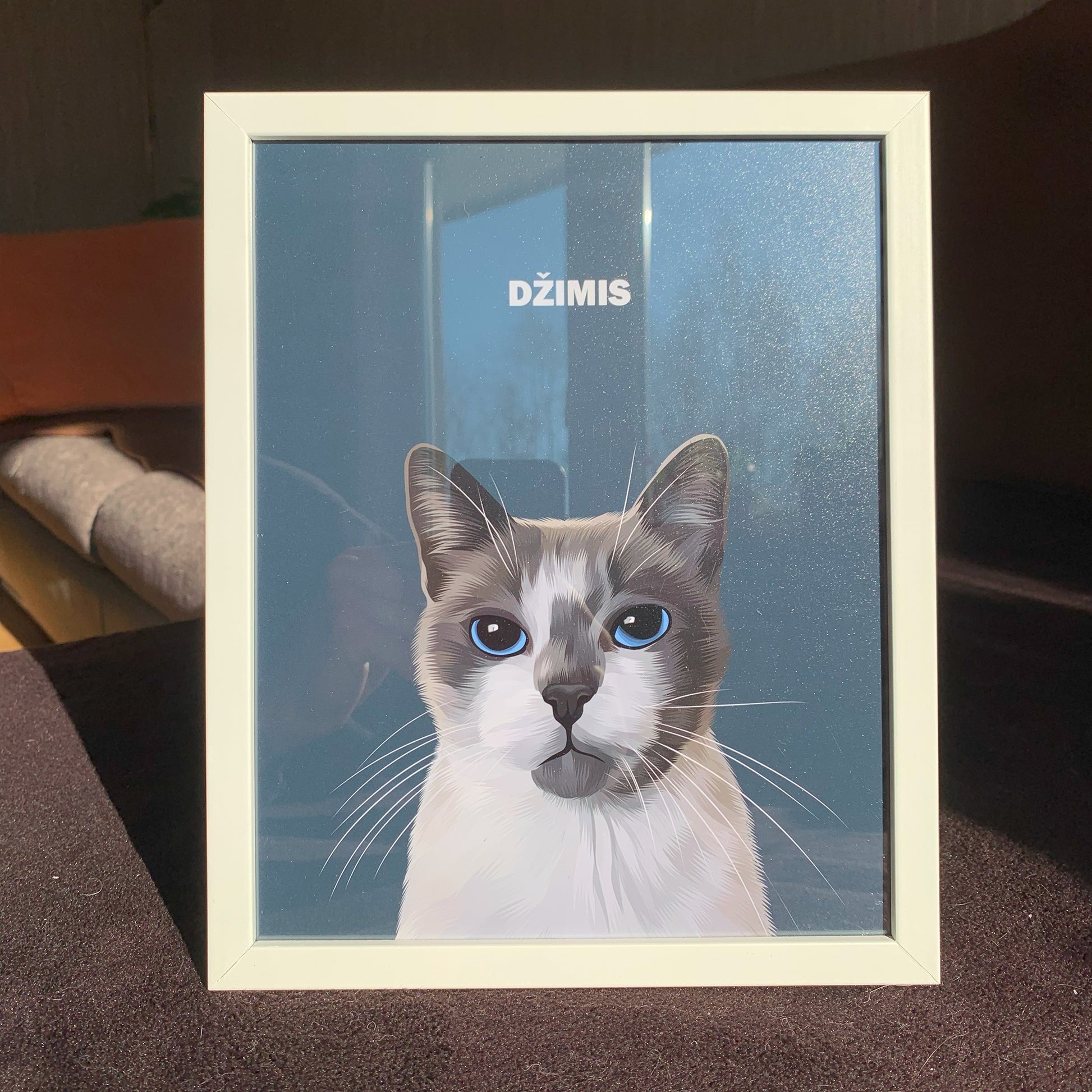 Close up photo of charcoal custom pet portrait framed poster with white and grey cat's artwork on it, framed in white frame, called Džimis