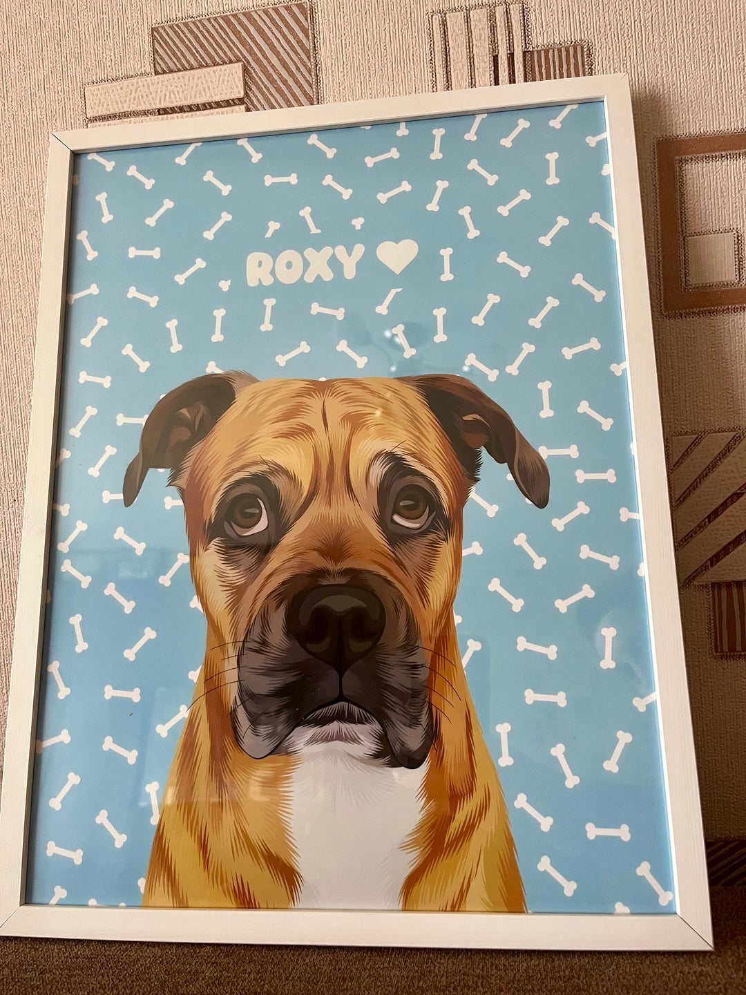 A framed custom cartoon-style portrait of a brown dog named Roxy, illustrated on a blue background with white bone patterns
