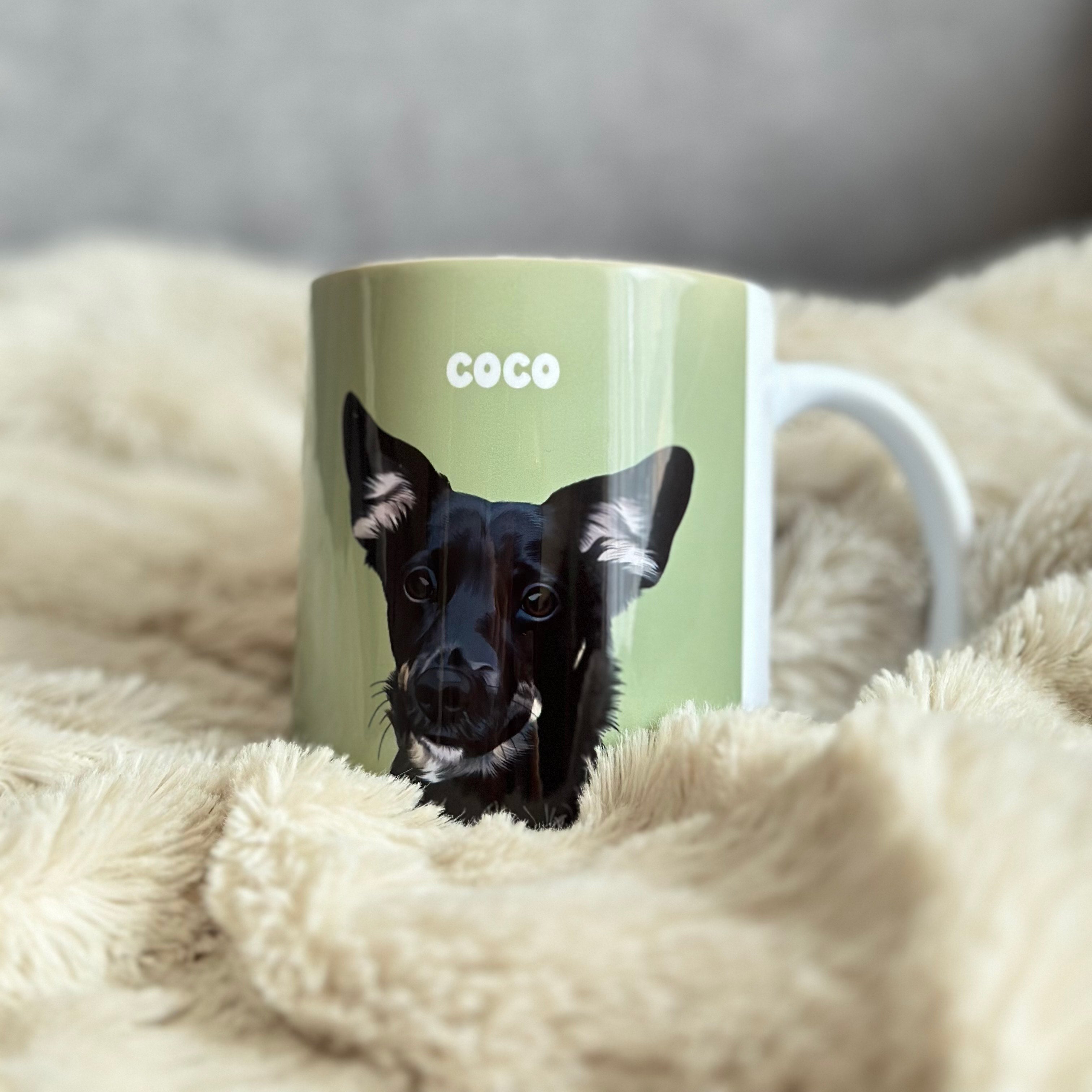 Close-up photo of custom pet portrait ceramic mug with black dog's artwork on it laying in sofa