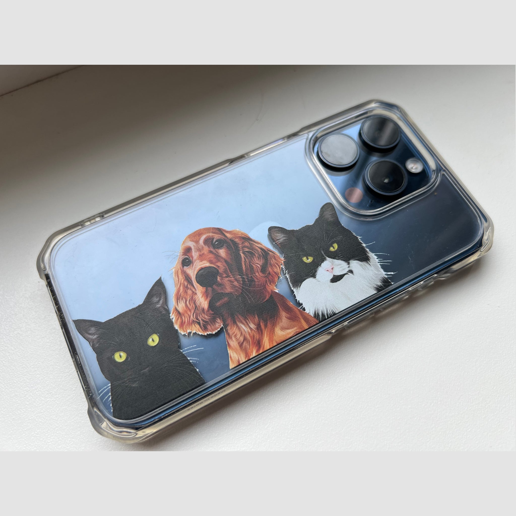 Close-up photo of transparent custom pet portrait phone case featuring 2 cats and 1 dog